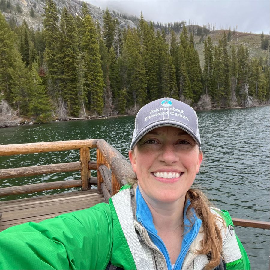 Selfie on a wooden dock by a mountain lake, wearing an “Ask me about Embodied Carbon” cap